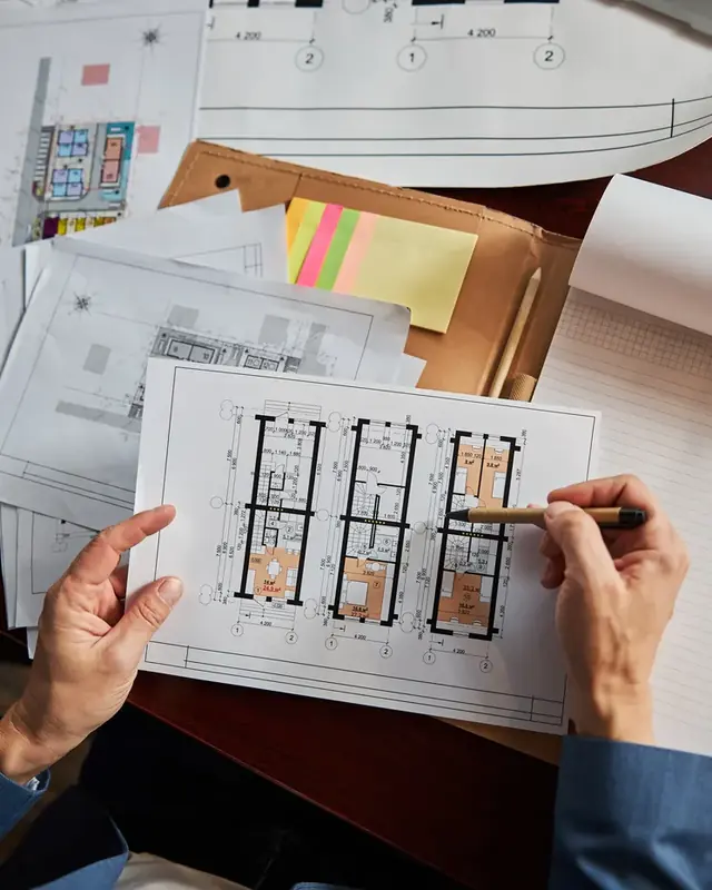 Overhead view of hands reviewing floor plans and documents at a desk.